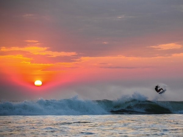 A guy surfing on the Nicaraguan sea during sunset